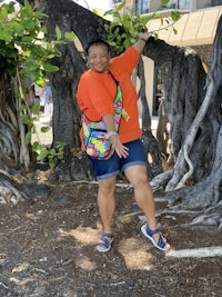 a woman in an orange shirt leaning against a tree