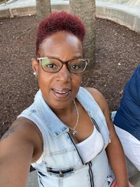 a woman wearing glasses and a denim vest is taking a selfie